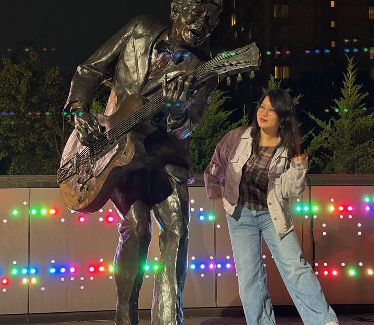 Ziyi next to a guitarist statue under string lights